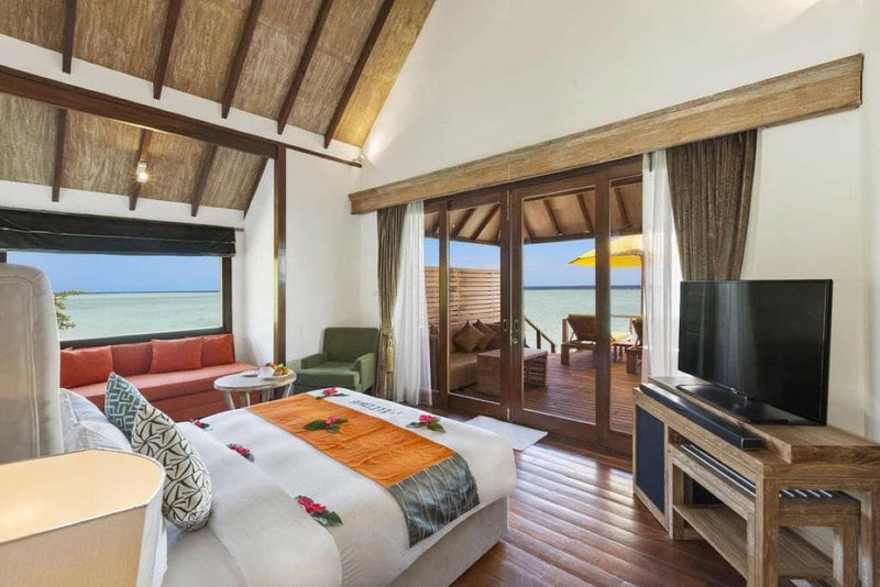 A Semi Water Villa bedroom at Dhigufaru Island Resort, red petals on the bed and a parasol outside.