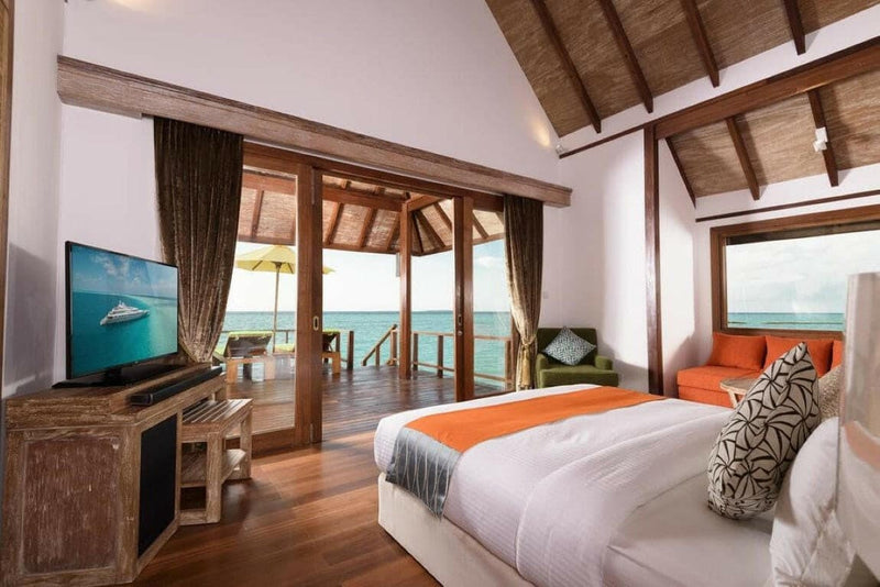 A villa bedroom at Dhigufaru Island Resort, patterned cushions and a red sofa on the deck beyond.