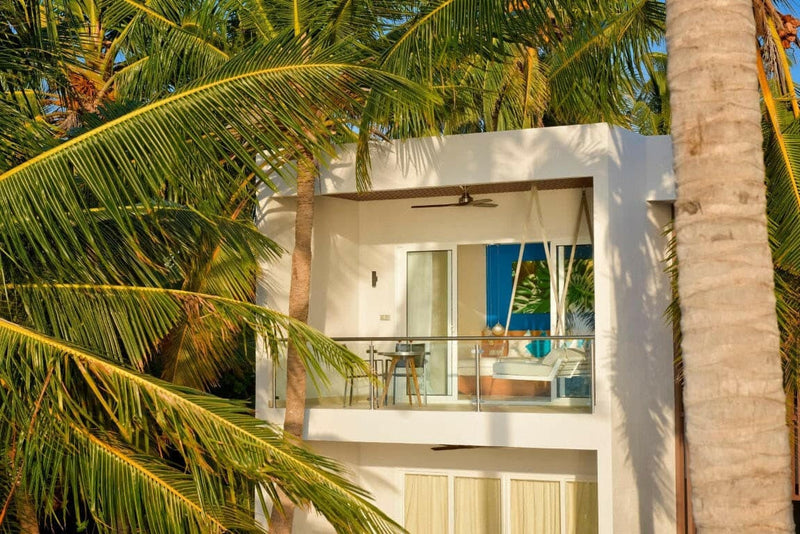 An upper balcony at Kandima Maldives framed by palm fronds, table and chairs against a blue wall.