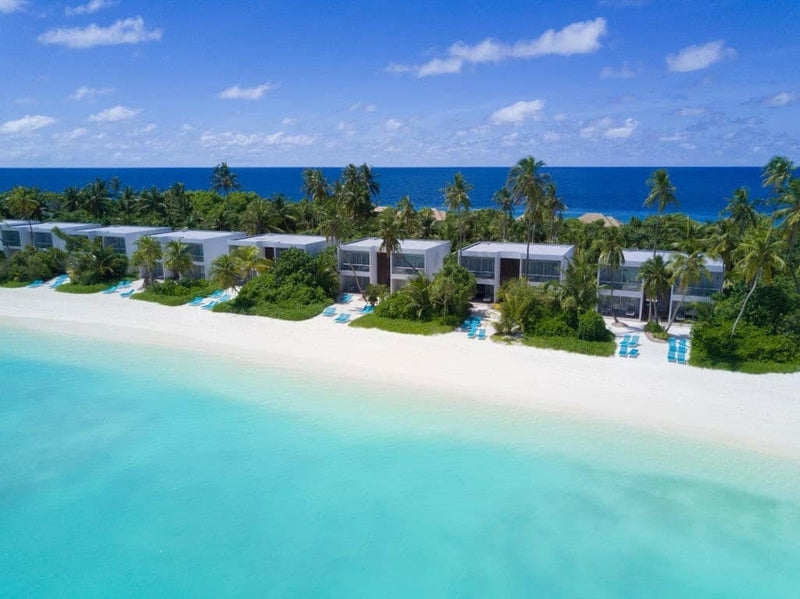 Kandima Maldives from the air, white studio blocks and pools set back from turquoise shallows.