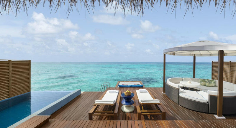An overwater terrace at W Maldives, twin loungers and a round canopied daybed beside the pool.