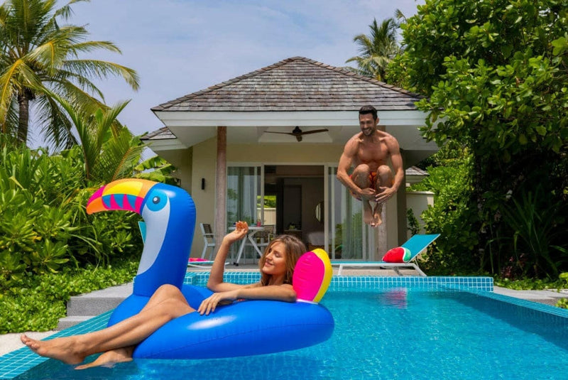 Guests at a villa pool at Kandima Maldives, one on a blue toucan float, one poised to dive in.