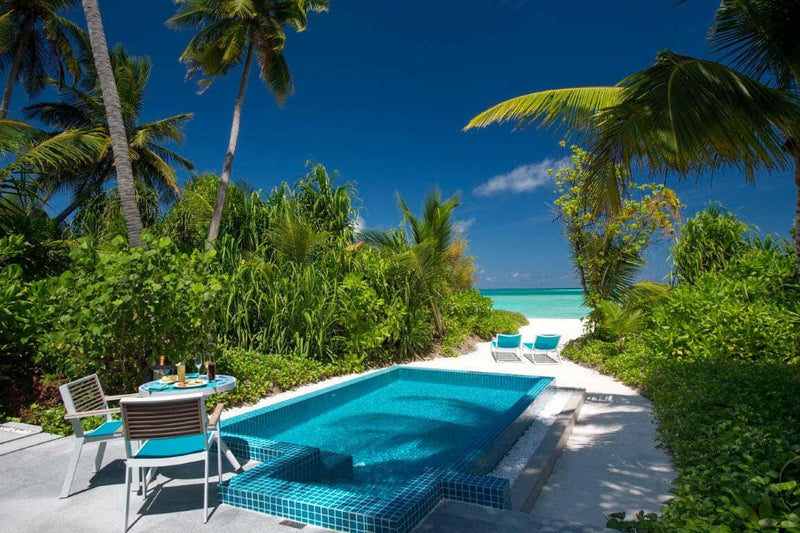 A villa pool at Kandima Maldives with loungers and a parasol, the sea just beyond the palms.