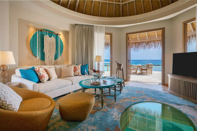The living room of a house at The Nautilus Maldives, cream sofas and tan armchairs with the doors open to the sea