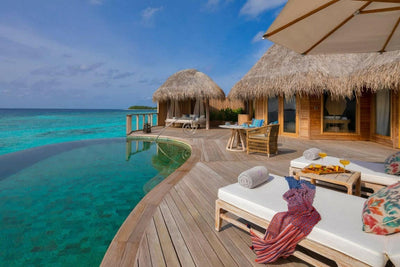 The deck of a house at The Nautilus Maldives, loungers and a parasol beside the curved infinity pool