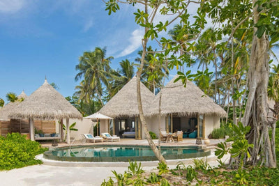 A Beach House at The Nautilus Maldives, thatched pavilions around a curved pool beneath old trees