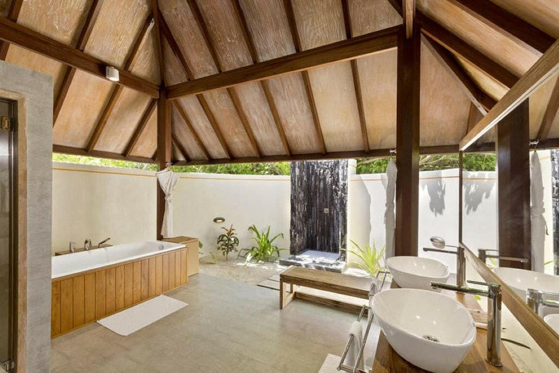 A villa bathroom at Dhigufaru Island Resort, timber clad tub and twin oval basins open to the sky.