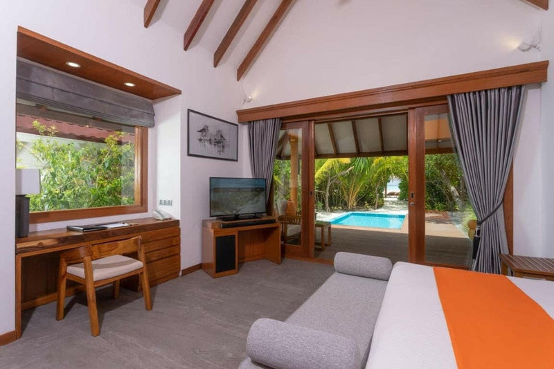 A villa bedroom at Dhigufaru Island Resort, desk and sofa with a turquoise pool through the doorway.