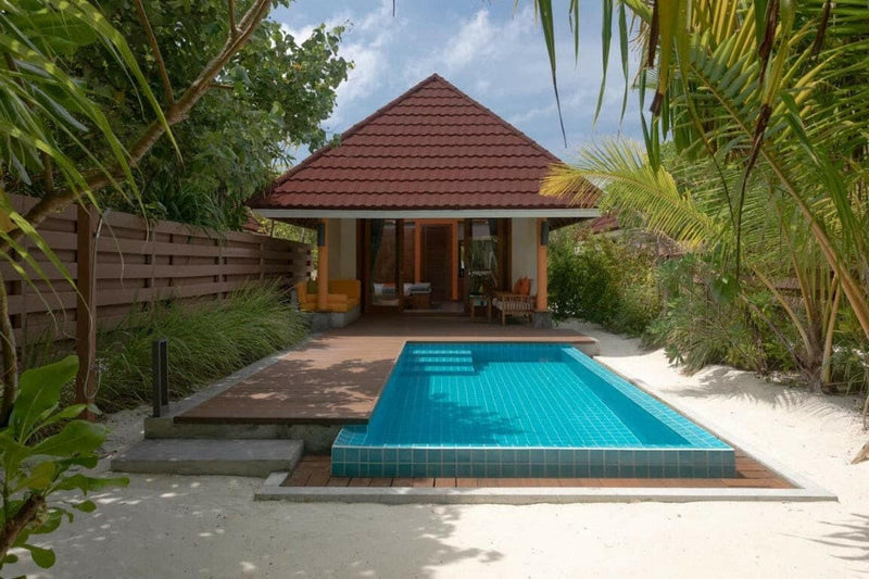 A beach villa at Dhigufaru Island Resort, long turquoise pool on sand below a red tiled roof.