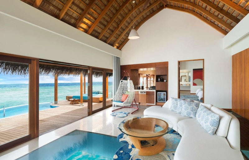 A villa living room at W Maldives, curved white sofa facing doors onto the pool deck.