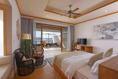 A Water Villa bedroom at Brennia Kottefaru, armchairs beside doors opening over the lagoon