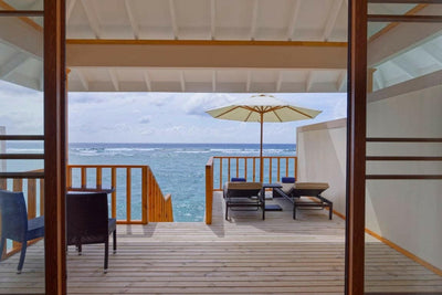 The deck of a Water Villa at Brennia Kottefaru, loungers and a parasol above the sea