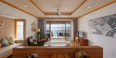 A Water Villa at Brennia Kottefaru, a daybed by the window and doors onto the deck
