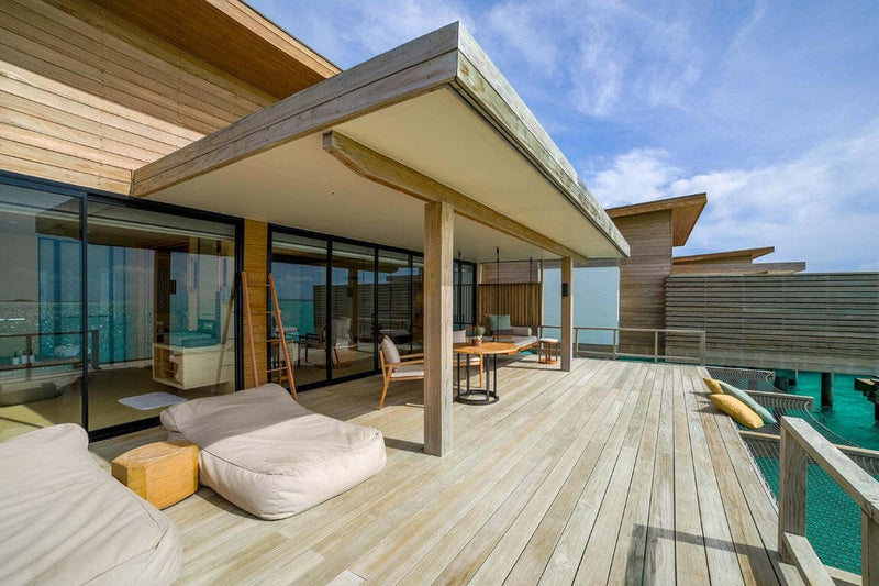 The pale timber deck of a water villa at Kuda Villingili, a low daybed beside the plunge pool.
