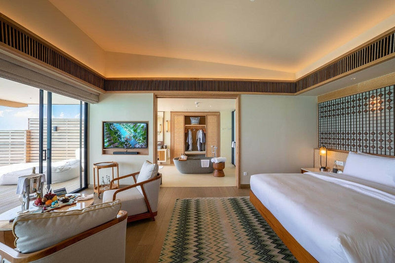 A villa bedroom at Kuda Villingili, white bed, patterned rug and a bathtub through the doorway.