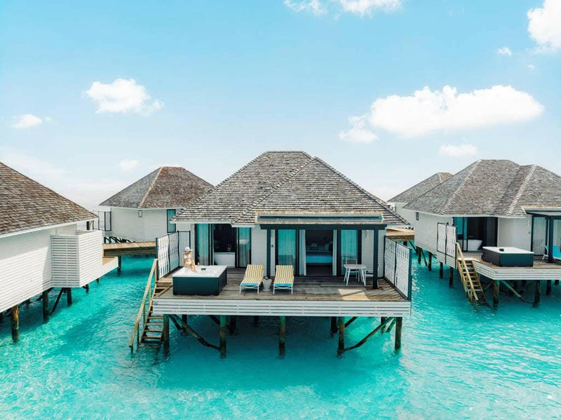 Thatched villas on stilts at Nova Maldives, seen from the lagoon with decks and jacuzzi tubs.
