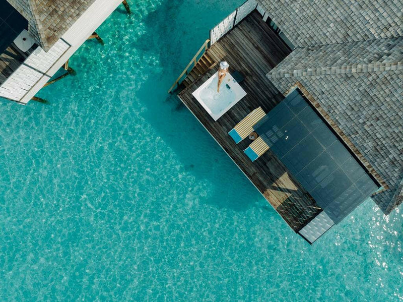 A guest lying in the deck jacuzzi of a water villa at Nova Maldives, turquoise water below.