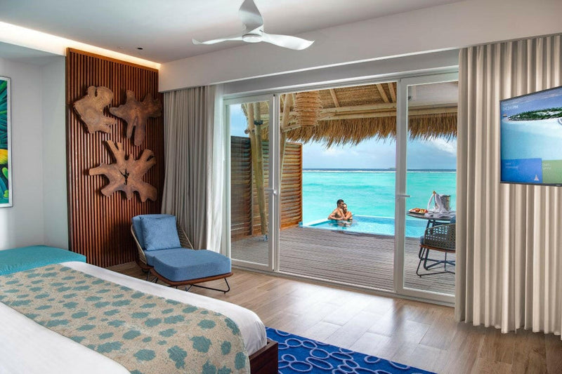 A water villa bedroom at Emerald Maldives, blue lounge chair and a deck pool at the lagoon edge.