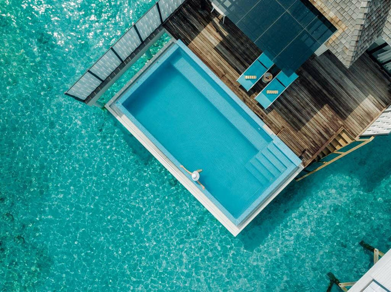 Looking down on a water villa plunge pool at Nova Maldives, a swimmer and two turquoise loungers.