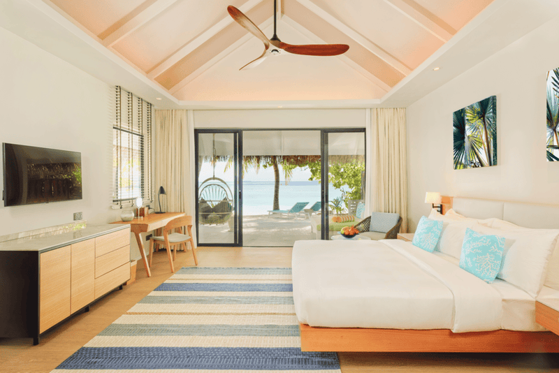 A villa bedroom at Nova Maldives, vaulted timber ceiling and sliding doors open to a deck and the sea.