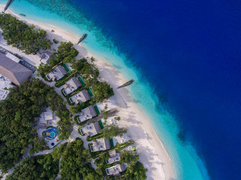 Emerald Maldives from the air, beach villas and their pools tucked behind the sand and drop off.