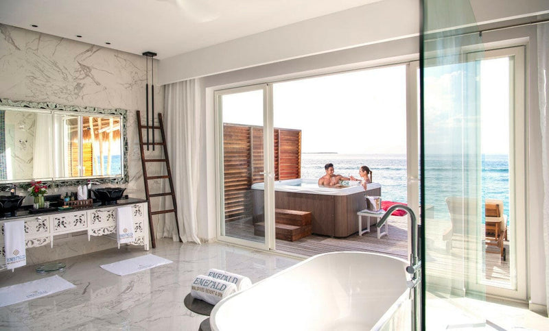 A villa bathroom at Emerald Maldives, marble walls and twin basins looking out to a deck hot tub.